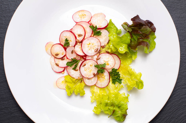 Υγιεινά τρόφιμα βιολογικά φέτες ραπανάκι σαλάτα στο άσπρο πιάτο σε μαύρο - Φωτογραφία, εικόνα