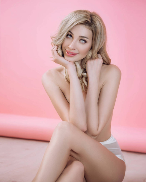 Sexy blonde girl in white panties sitting in studio on a pink background - Photo, Image