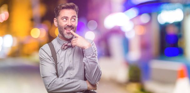 Мужчина среднего возраста, с бородой и галстуком-бабочкой уверенный и счастливый с большой естественной улыбкой смеющийся в ночном клубе
 - Фото, изображение