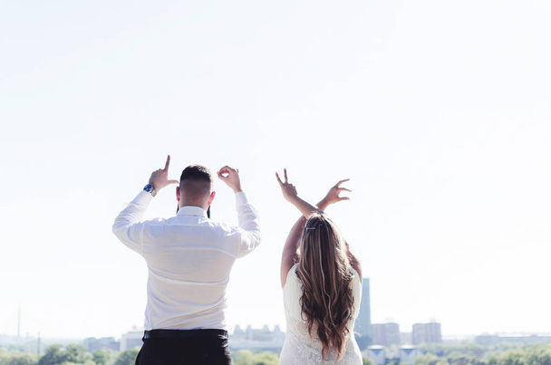 Backs of wedding couple on cliff, showing love word with fingers - Foto, immagini
