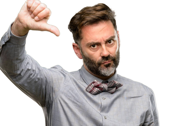 Мужчина средних лет, с бородой и галстуком-бабочкой показывает пальцы вниз несчастный признак неприязни, негативное выражение и неодобрение изолированы на белом фоне
 - Фото, изображение