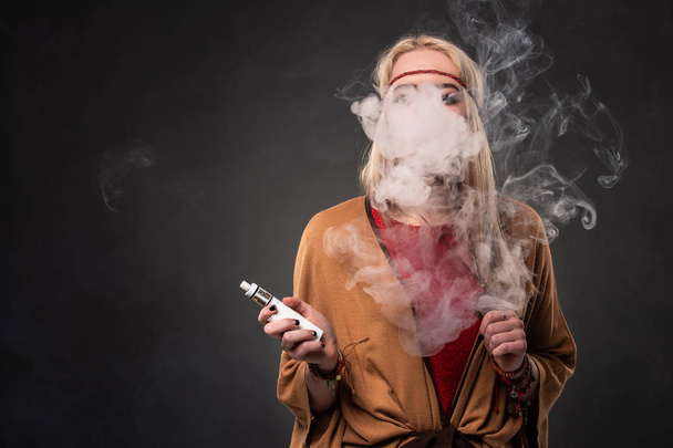 セクシーな若いヒップな喫煙 vaping 女の子の肖像画。女性は、自由奔放に生きるのスタイルに身を包んだ。蒸気のコンセプトです。Vaping 電子タバコ. - 写真・画像