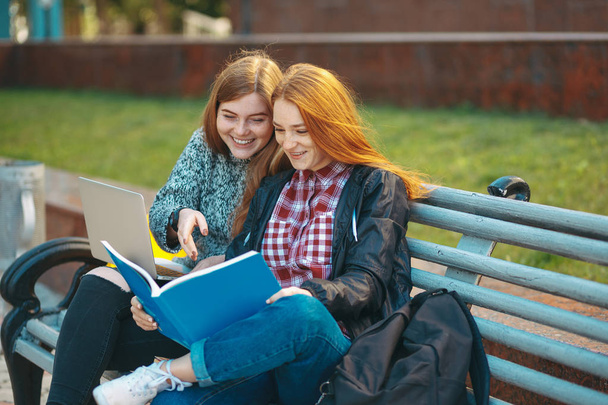 Dwóch studentów siedzieć na ławce patrząc w książce i uśmiechając się - Zdjęcie, obraz