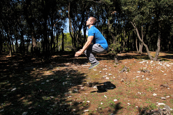 muskulöser Mann beim Workout springen in der Luft Übung im Wald. Der gut aussehende Sportler in Sportkleidung springt beim Lufttraining in der Natur im Freien auf. Cross-Fit, gesundes Lebensstilkonzept. - Foto, Bild
