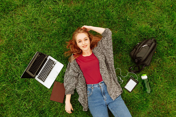 Jeune femme blonde souriante étudiante allongée sur l'herbe à l'extérieur
 - Photo, image