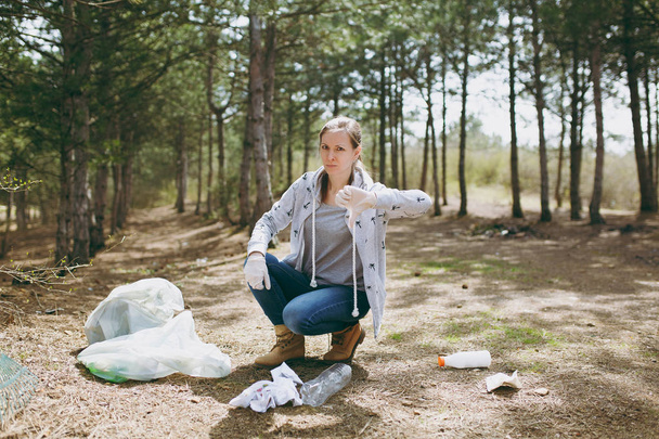 Молодая расстроенная женщина в повседневной одежде и перчатках убирает мусор
  - Фото, изображение