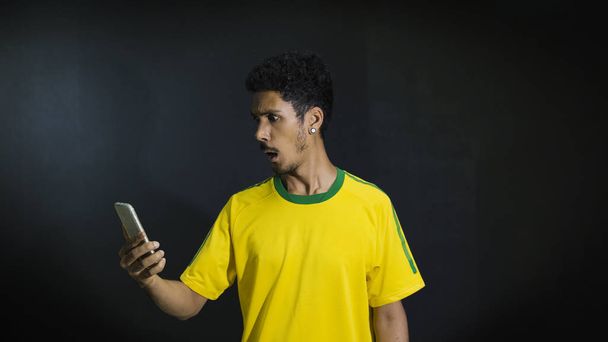 Αρσενικό αθλητής ή ανεμιστήρα σε κίτρινο ομοιόμορφη ψάχνει κινητό τηλέφωνο στον blac - Φωτογραφία, εικόνα