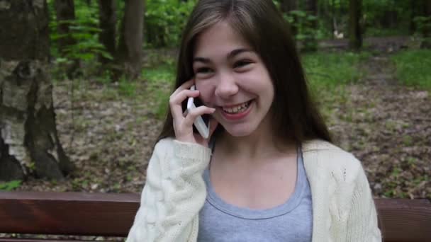 Young attractive girl speak to phone on bench. Summer park. Smile. HD video footage shooting static camera. - Materiaali, video