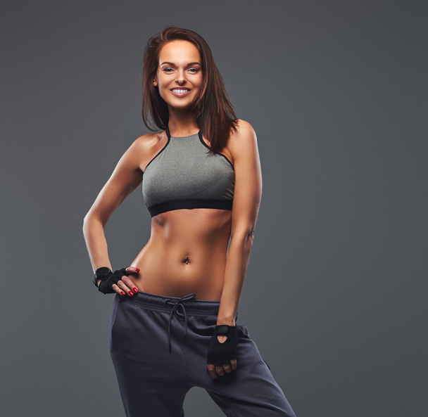 Sonriente morena fitness mujer en una ropa deportiva gris posando en un estudio
. - Foto, imagen