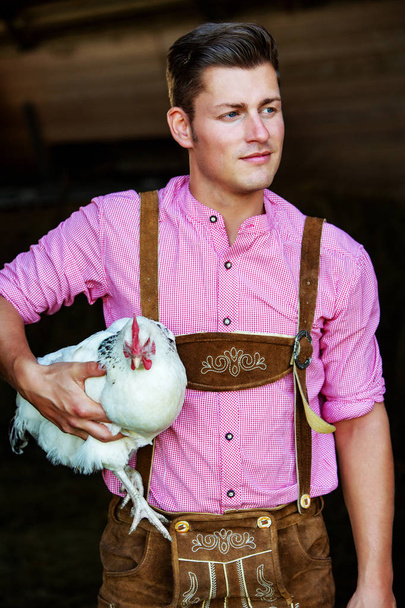 young bavarian man holding a white chicken - Фото, изображение