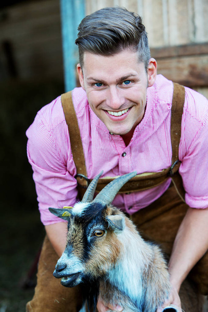 young bavarian man holding a goat - Фото, изображение