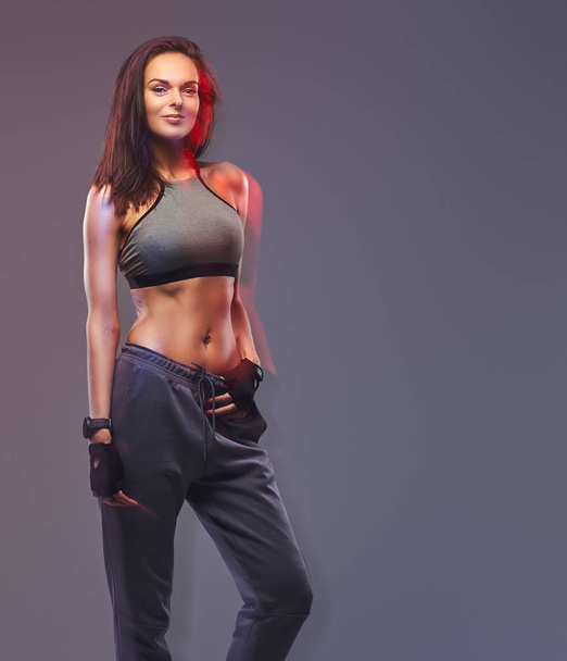 schlanke Fitness brünette Frau in grauer Sportbekleidung posiert in einem Studio. - Foto, Bild