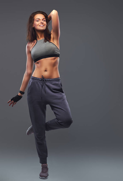 Smiling fitness brunette woman in a gray sportswear posing in a studio. - Photo, Image