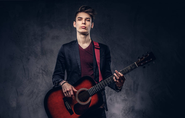 Elegante joven músico con el pelo elegante en ropa elegante, tocando en una guitarra acústica
. - Foto, imagen
