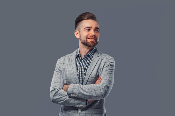 Smiling stylish man in an elegant gray suit, posing with crossed arms in a studio. - Photo, Image