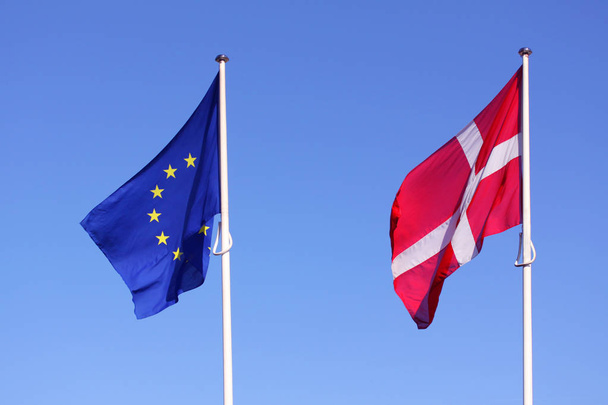 Evropské unie Eu a dánské vlajky pro Dánsko na tyči mávat ve větru s modré oblohy za slunečného dne jako pozadí - Fotografie, Obrázek