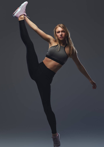 Beautiful blonde girl stretches her legs before training. - Photo, Image