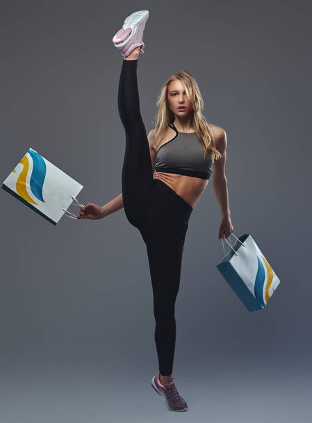 Beautiful blonde girl lifts foot above head with packages in the hands. - Photo, Image