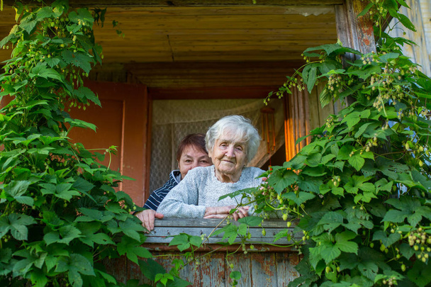 Oudere vrouw met haar volwassen dochter op de veranda van een boerderij. - Foto, afbeelding