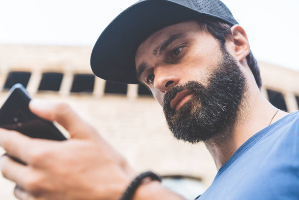 Young handsome bearded man using his smartphone on the street. Blurred background. Horizontal. - Fotoğraf, Görsel