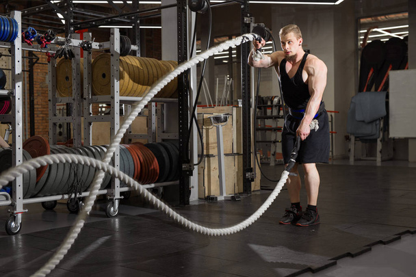 a handsome man with a beard is engaged in exercises with ropes in the gym - Foto, Imagen