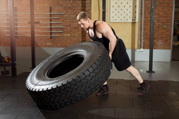 beautiful man with a beard pulling a heavy wheel in the gym - Photo, image