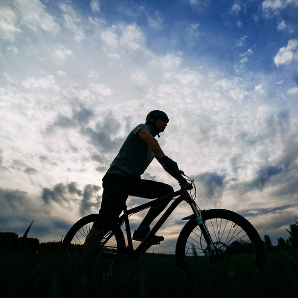 Hombre montar en bicicleta sobre el fondo del cielo puesta del sol
 - Foto, Imagen