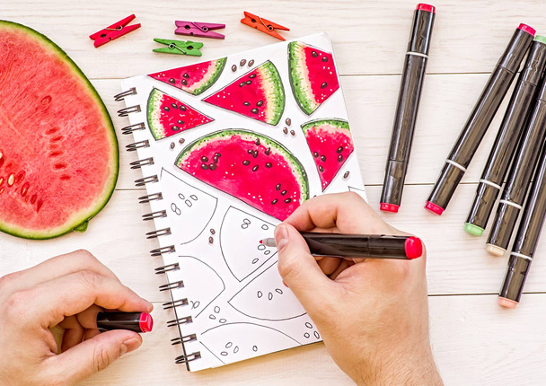 mãos de homem desenhando um esboço de melancia em fundo de madeira com marcadores
 - Foto, Imagem
