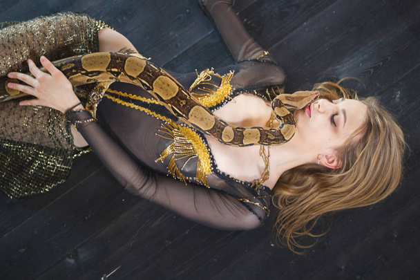 Joven rubia tumbada en el suelo con una serpiente en la cara en un estudio
 - Foto, Imagen