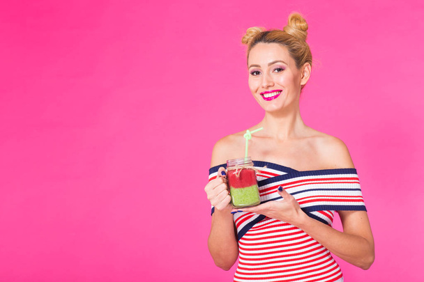 Retrato de la divertida joven con traje brillante, sosteniendo y bebiendo sabroso batido verde batido sobre fondo rosa con copyspace
 - Foto, imagen