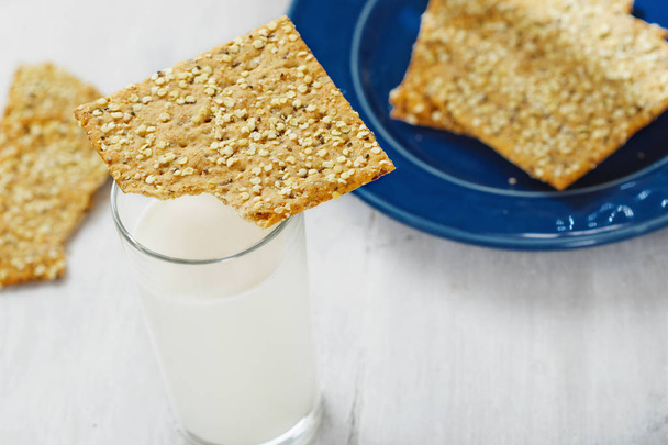 Fitness cookies with chia seeds, flax and pumpkin on white wooden background with glass milk - Fotó, kép