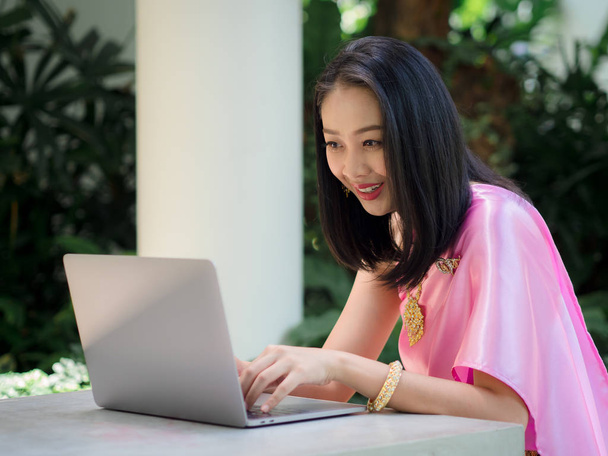 Thai woman in traditional costume is using a laptop in the garde - Photo, image