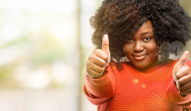 Красивая африканская женщина стоит счастливой и позитивной с большими пальцами вверх одобряя с большой улыбкой выражая хорошо жеста, на открытом воздухе
 - Фото, изображение