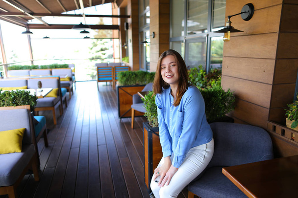 Girl sitting in arm chair at cafe near room plants and table. - Photo, Image