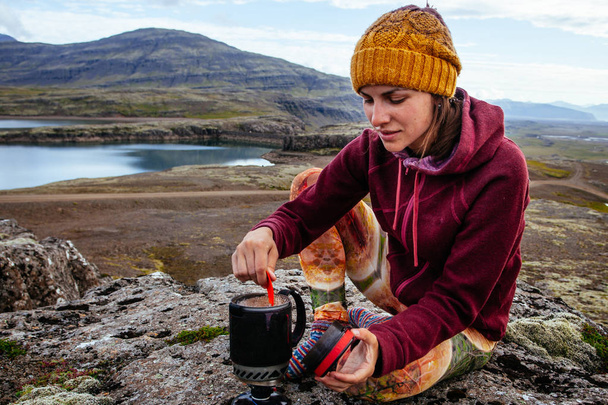 Mujer joven en ropa turística haciendo café en la naturaleza en
 - Foto, Imagen