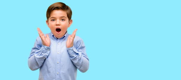 Knappe peuter kind met groene ogen blij en verrast juichen waarin wow gebaar op blauwe achtergrond - Foto, afbeelding