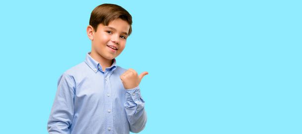 Красивый ребенок с зелеными глазами, указывающими в сторону с пальцем на синем фоне
 - Фото, изображение