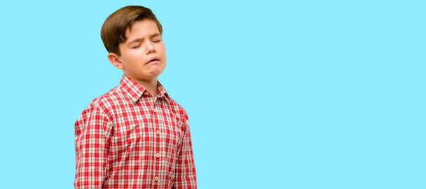 gutaussehendes Kleinkind mit grünen Augen weint deprimiert voller Traurigkeit und drückt traurige Gefühle vor blauem Hintergrund aus - Foto, Bild