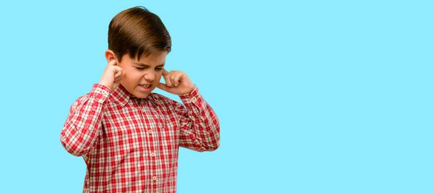 Όμορφος νήπιο παιδί με πράσινα μάτια που καλύπτουν τα αυτιά αγνοώντας ενοχλητικό δυνατό θόρυβο, βύσματα αυτιά για να αποφευχθεί η ακρόαση ήχου. Θορυβώδης η μουσική είναι ένα πρόβλημα. σε μπλε φόντο - Φωτογραφία, εικόνα