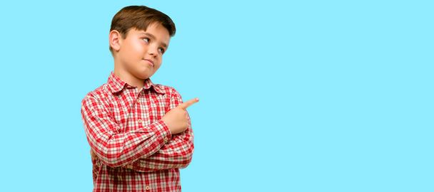 Handsome toddler child with green eyes pointing away side with finger over blue background - Фото, зображення