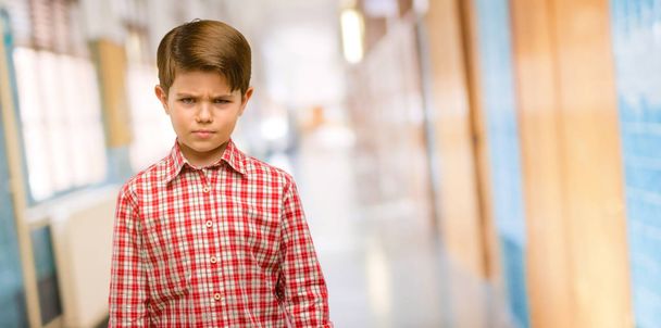 Pěkný batole dítě se zelenýma očima, podrážděný a vzteklý, vyjadřuje negativní emoce, otrávený s někým na školní chodbě - Fotografie, Obrázek