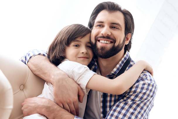 Bearded father embraces with teenager son sitting on the couch. - 写真・画像