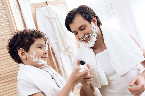 Joyful father inserts shaving foam onto hands of young son. - Valokuva, kuva