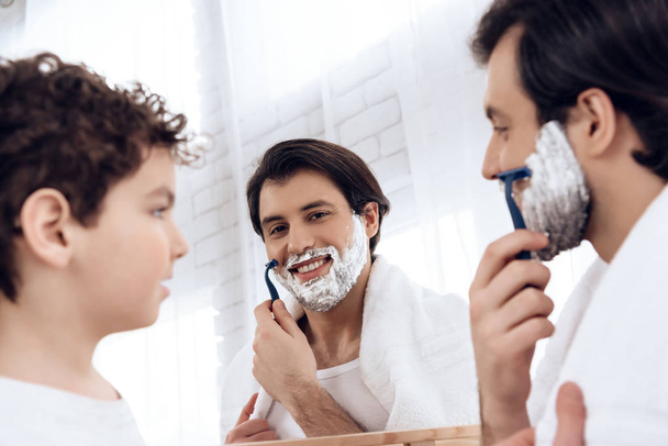 Little son looks like father shaves beard with razor. - Fotó, kép