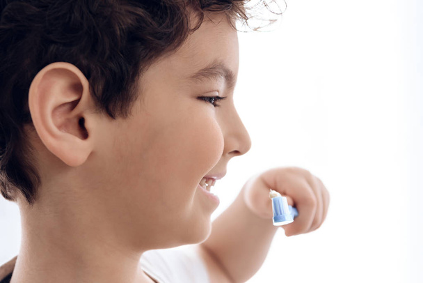 Close up. Joyful boy brushes teeth with toothpaste on white background. - Foto, immagini