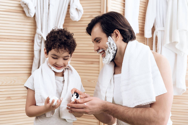 Joyful father inserts shaving foam onto hands of young son. - Fotoğraf, Görsel