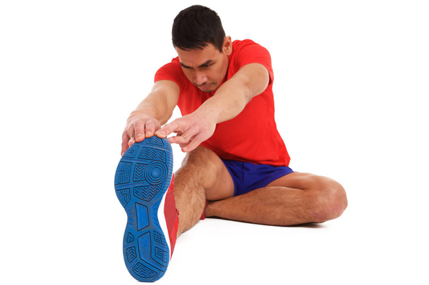 Portrait of middle aged man doing stretching exercise on white background, sitting and toughing his toes. - Photo, Image