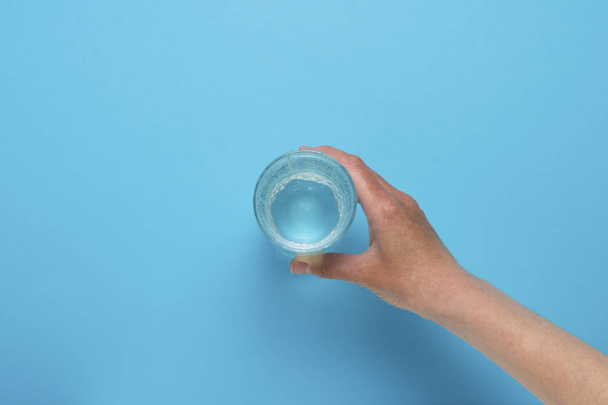 Female hand taking a glass of water on a blue background. Flat L - Foto, imagen
