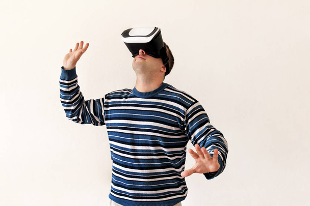 Человек носит и играет мобильное приложение игры на устройстве очки виртуальной реальности на белом фоне. Man action and using in virtual headset, VR box for use with smarphone. Концепция современных технологий
 - Фото, изображение