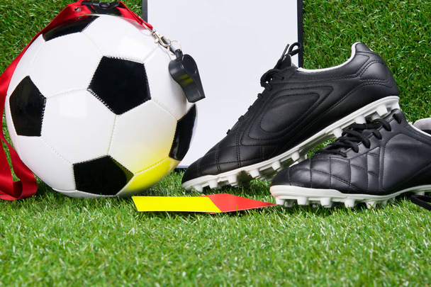 boots, a football ball, a writing pad, a whistle and penalty cards for a judge, against the background of grass - 写真・画像